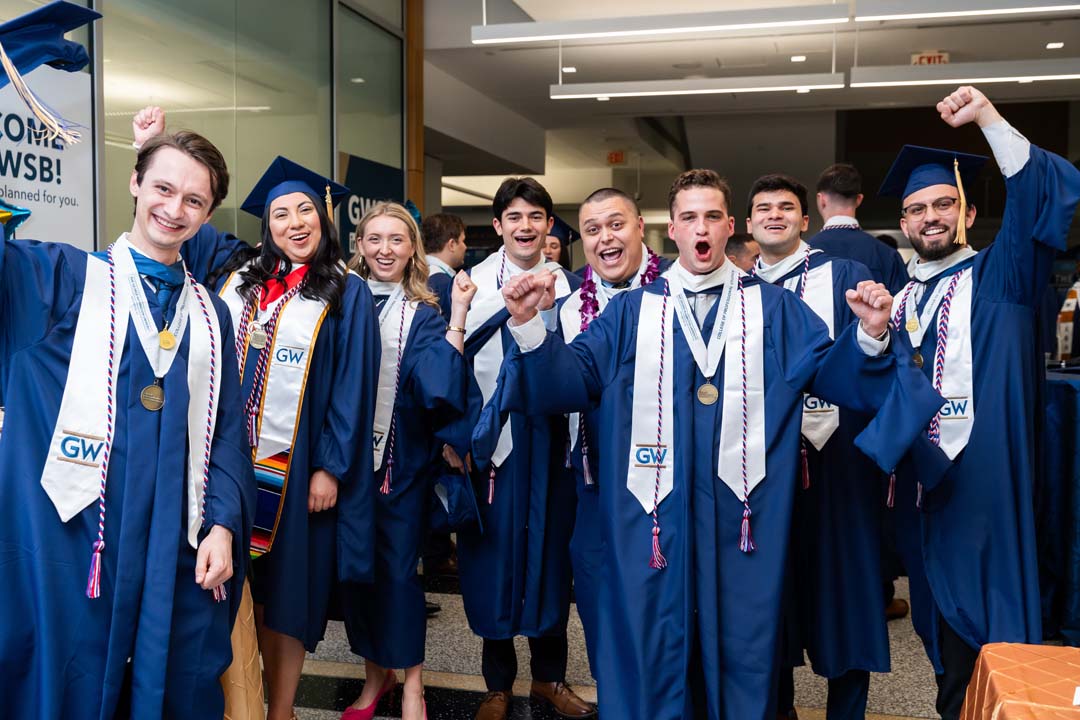 Students in cap and gowns pose excitedly after graduating.