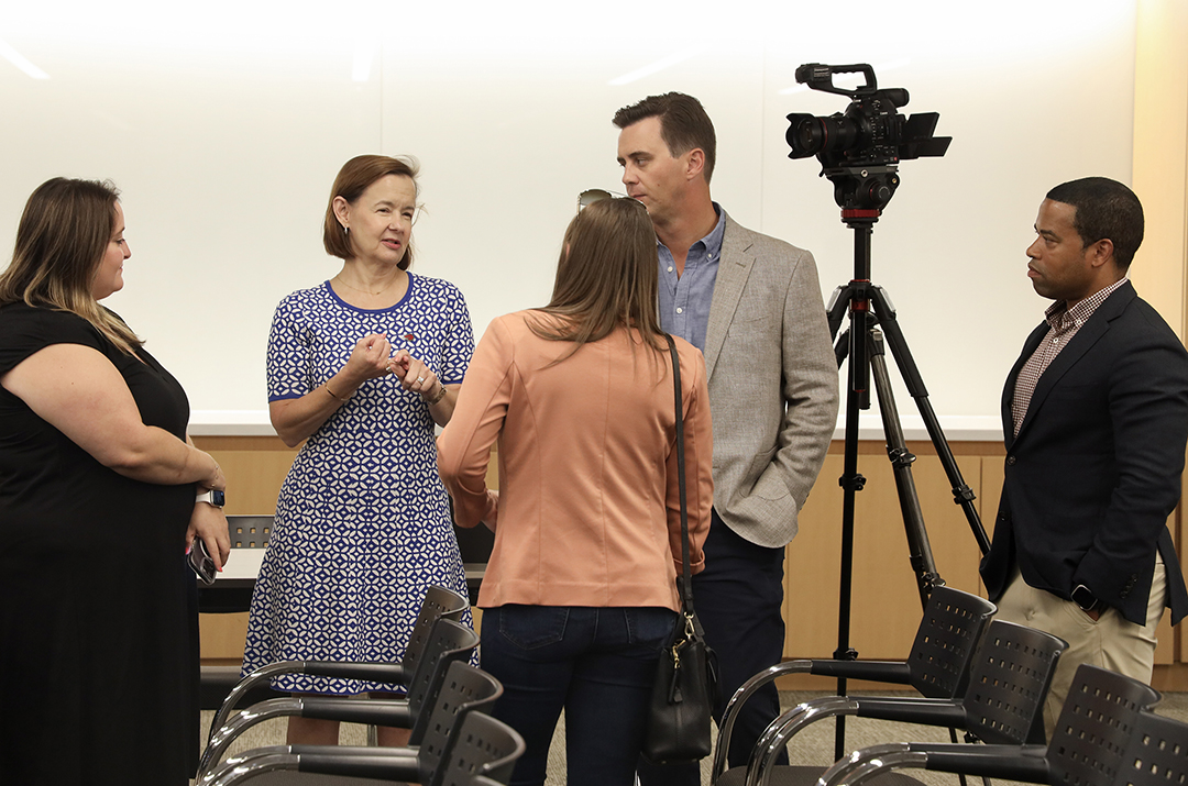 Group of 5 discussing, 3 women, 2 men and camera on tripod