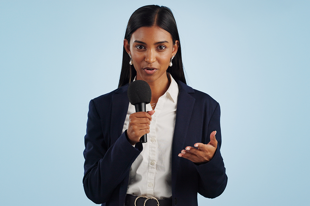 woman in blazer with long dark hair and a microphone on blue background