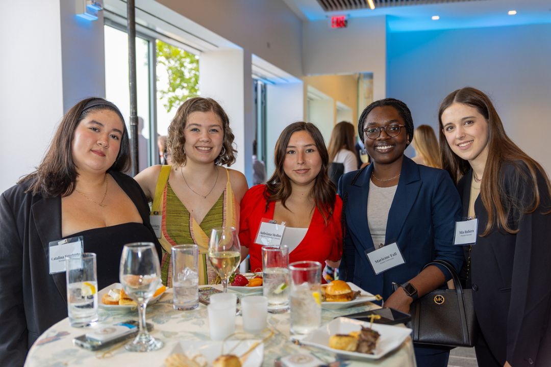 Students smile and pose around a table
