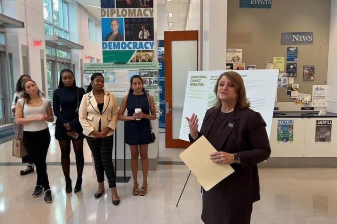 Dean Liesl Riddle speaking in the foreground while Capstone students listen in the background 