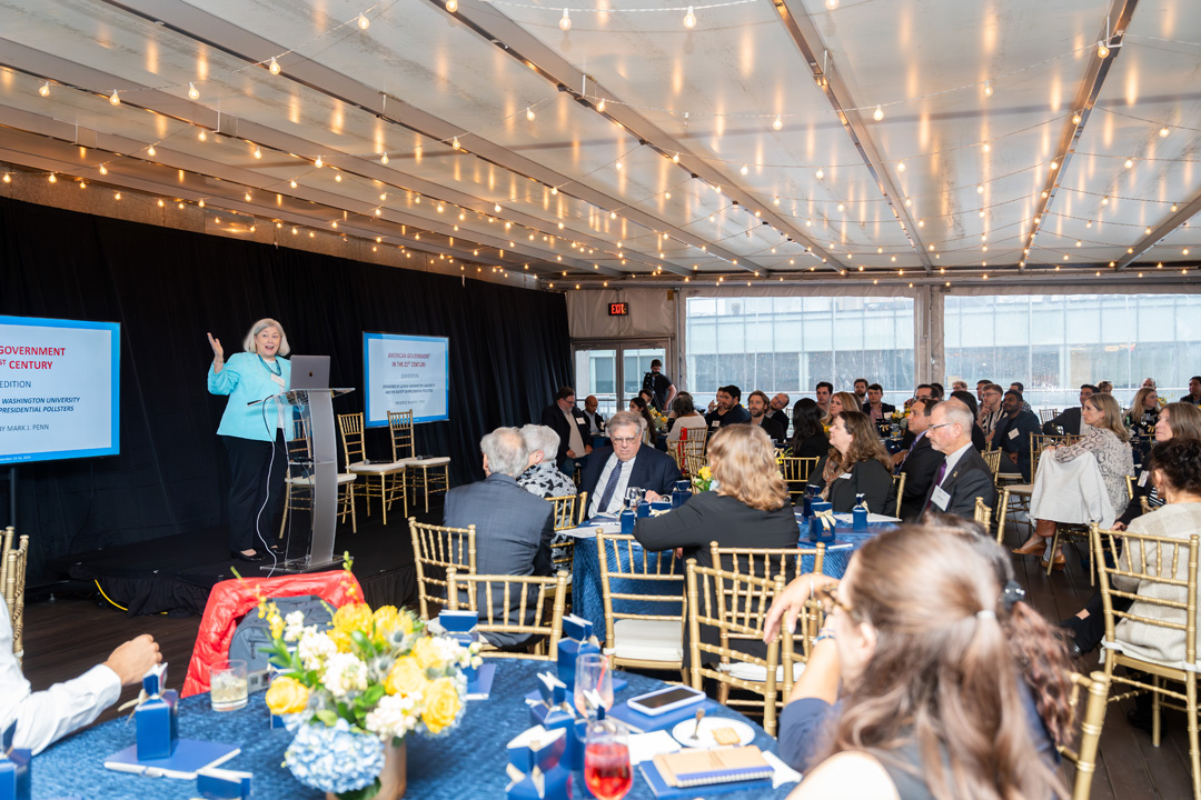 GW President Ellen Granberg standing onstage; the entire audience is visible, sitting at tables and listening to President Granberg speak.
