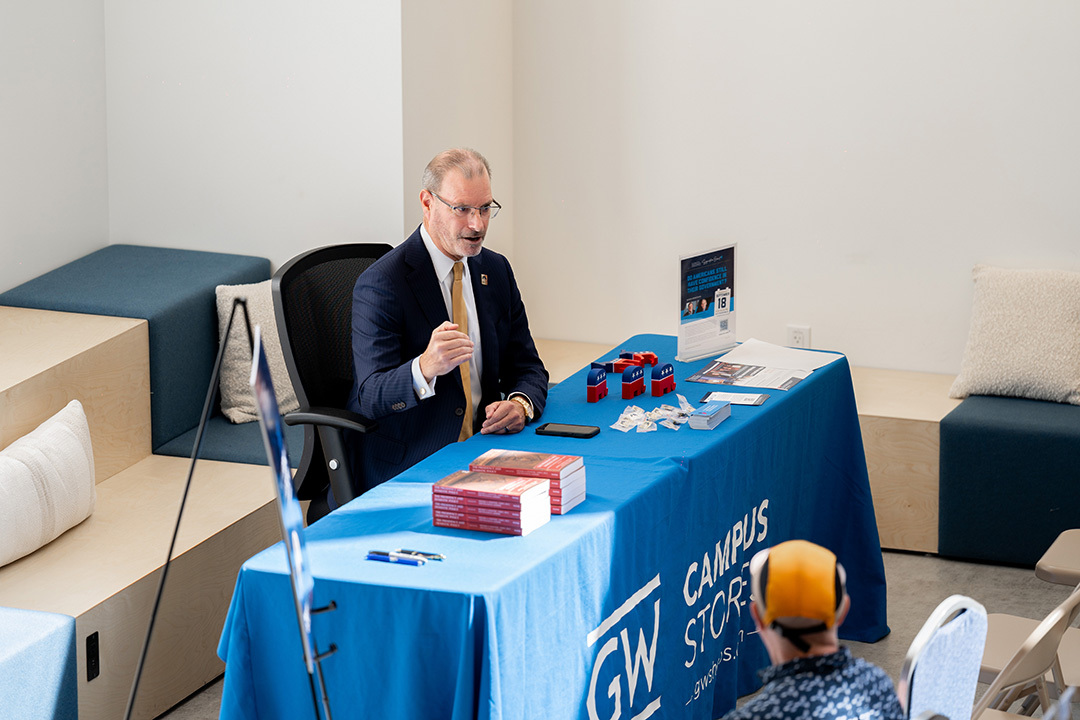 Todd Belt sitting at a GW campus store table, signing copies of his new book