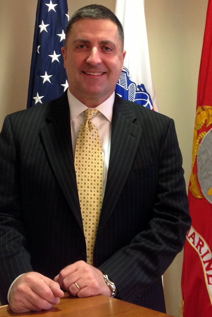 Sean Blochberger in dark suit with light tie and marine corp and us flag