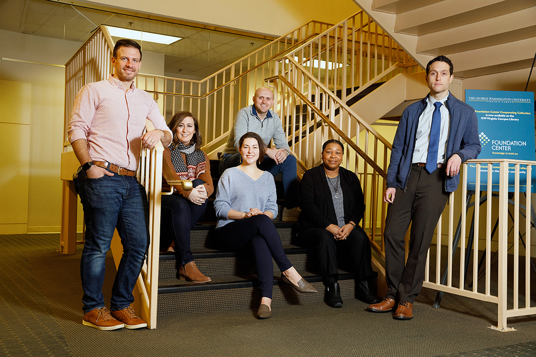 Photo with 6 people, mix of men and women, posing by staircase with metal railings