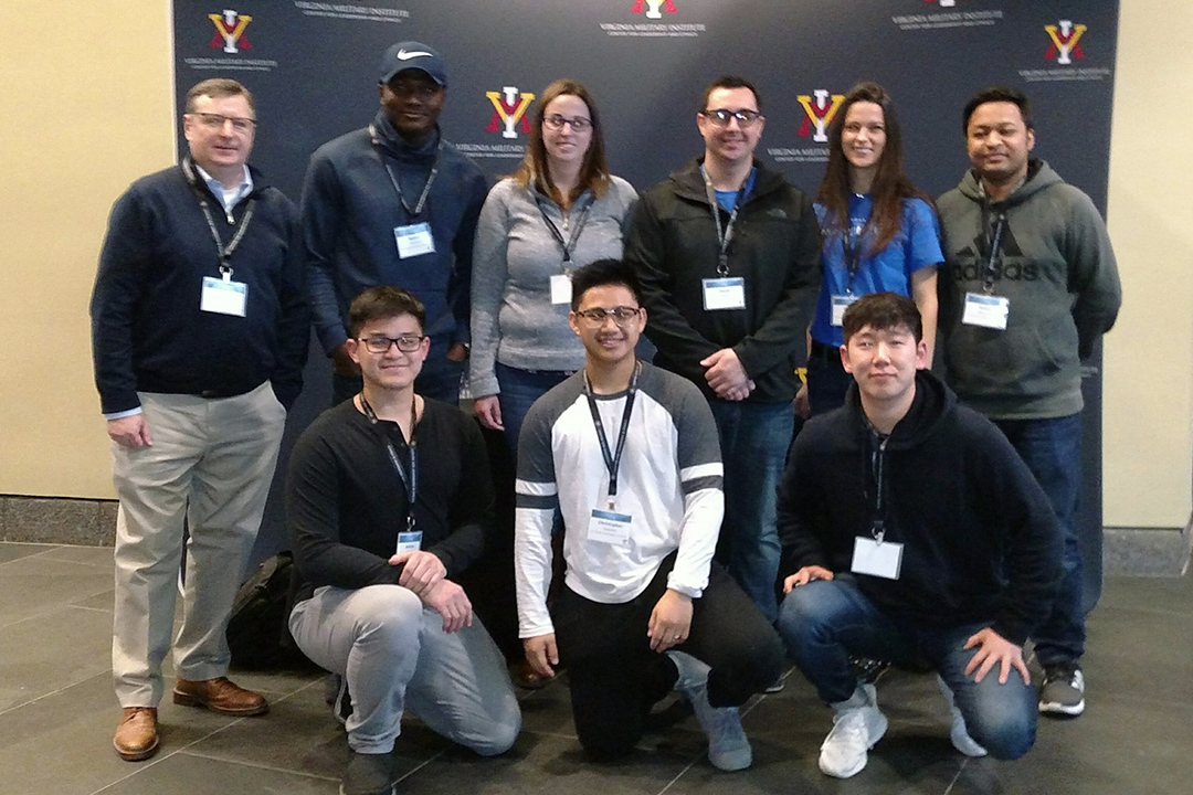 Group of 8 diverse students and 1 faculty member at the competition in a formal group photo.