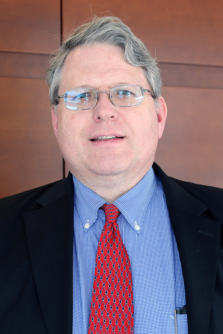 Man w/glasses, wavy hair, dk. blazer, red tie, blue collared shirt