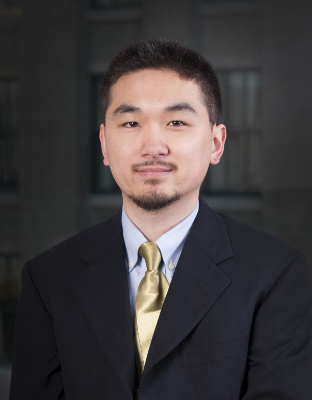 Man with small beard, dark short hair in dk.suit with lt. blue collared shirt and gold tie