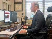 Dr. Todd Belt in a dark suit, white shirt and glasses in his office looking at a computer monitor watching Michael Cohen testify
