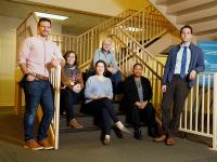 Photo with 6 people, mix of men and women, posing by staircase with metal railings