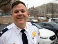Duncan Bedlion smiling with cars behind him in his police uniform with badge