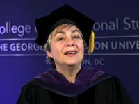 Toni Marsh wearing commencement gown and hat with tassel and part of College of Professional studies logo on a blue wall behind 