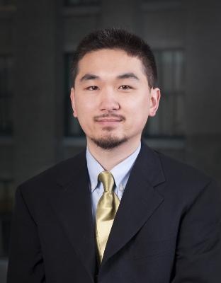 Man with small beard, dark short hair in dk.suit with lt. blue collared shirt and gold tie