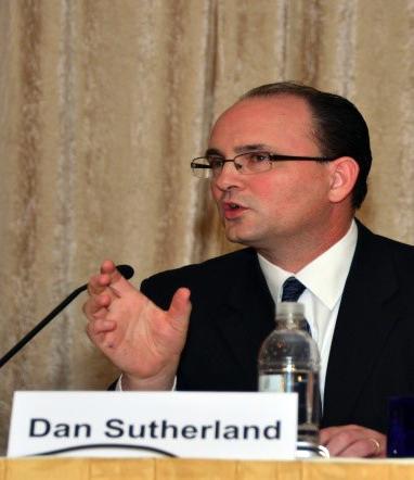 Sutherland in a suit talking with microphone