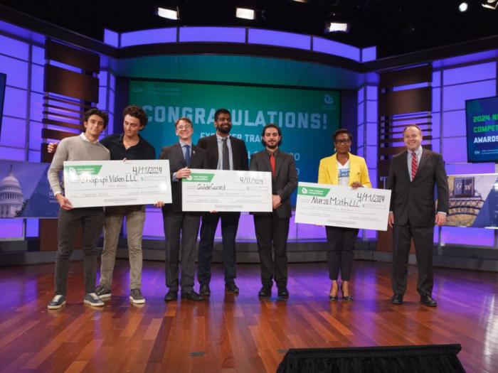 New Venture Competition winners standing onstage holding oversized checks