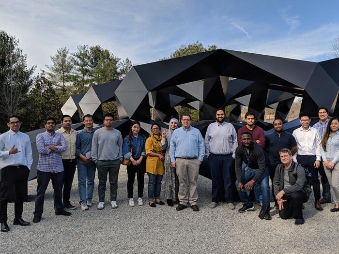 Large IIST student group of approximately 20 people in front of a black metal abstract sculpture