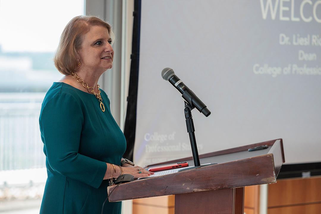 Dean Liesl Riddle speaking into a microphone at a podium