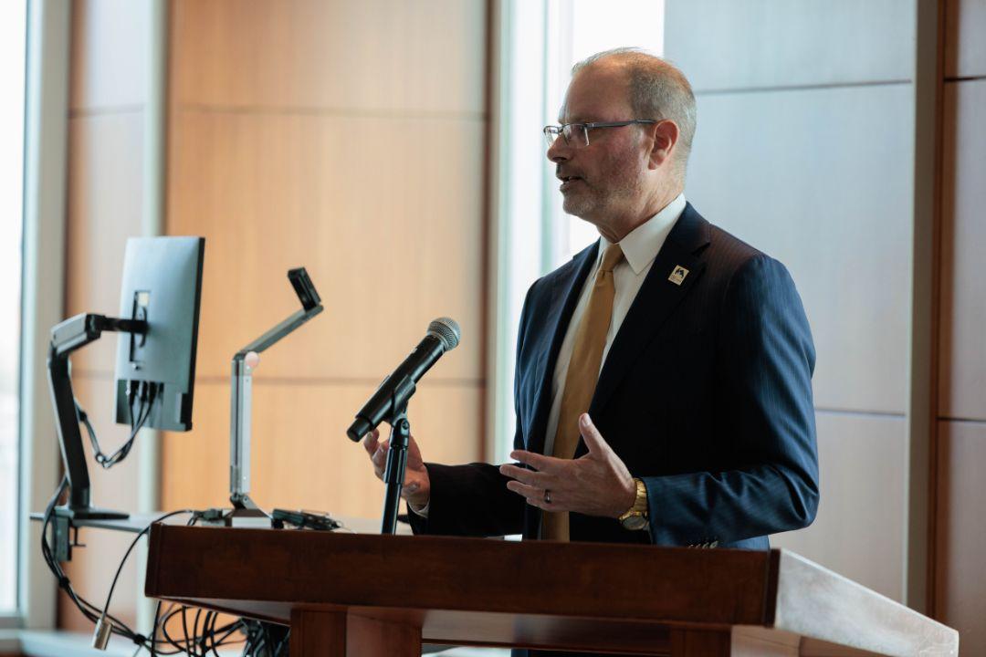 Dr. Todd Belt standing at a podium, speaking