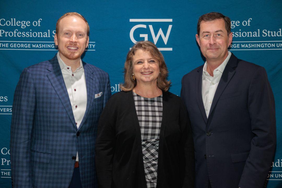Anthony Shop, Liesl Riddle, and Terry Szuplat smiling and posing in front of GW step-and-repeat
