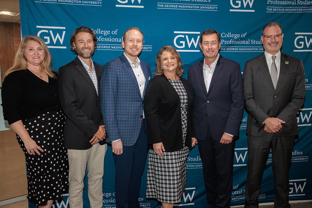 Lesley Lopez, Casey Burgat, Anthony Shop, Dean Riddle, Terry Szuplat, and Todd Belt smiling and posing in front of GW step-and-repeat