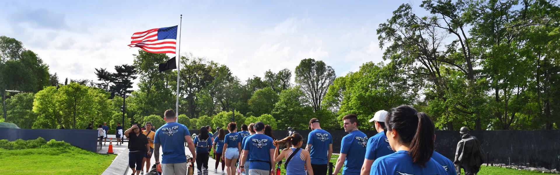 Military students with matching blue tshirts with logo visit memorial, US Flag, trees